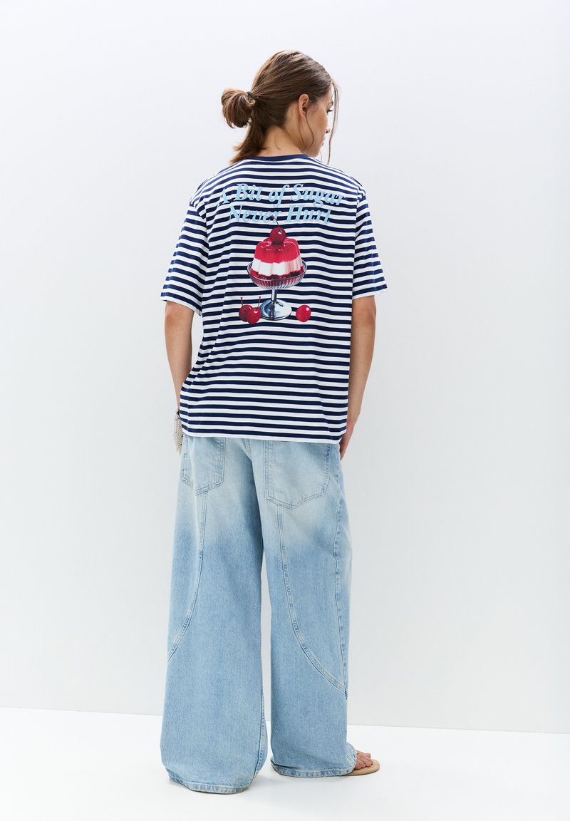 Stribet navy og hvid t-shirt med et stort, farverigt dessertmotiv på ryggen. Kombineret med løse, lyseblå denim jeans.