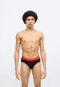 Μαύρα εσώρουχα με κόκκινη ελαστική μέση TOMMY HILFIGER. Το ύφασμα φαίνεται λείο και εφαρμόζει άνετα, με κλασική γραμμή εσώρουχου.