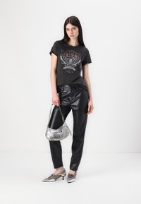 Grafische zwarte t-shirt met de tekst "LOVER", gecombineerd met glanzende zwarte leren broek. Een zilveren handtas en metallic schoenen maken de look compleet.