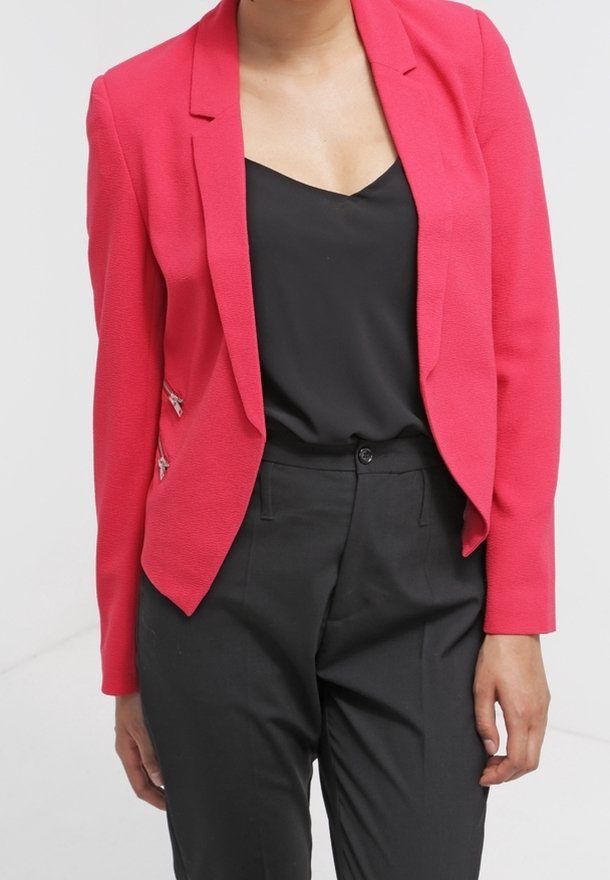 Blazer ajustado de color rosa con una tela texturizada, solapas muestradas y detalles en plata con cremallera, combinado con una blusa negra y pantalones negros a medida.
