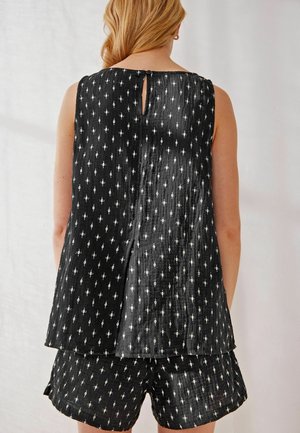 Czarny bezrękawnik z wycięciem na plecach, wykonany z teksturowanego materiału z powtarzającym się białym wzorem diamentów. Dobranie do tego spodenki w tym samym stylu.