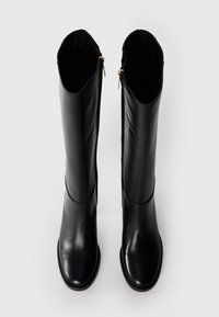 Bottes noires en cuir montantes avec une finition lisse, des fermetures éclair latérales et un design minimaliste, présentant une pointe arrondie et une semelle plate.