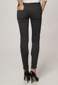 Smal svarta jeans med en slät yta, med två bakfickor och midjhög midja, ihop med svarta högklackade skor.