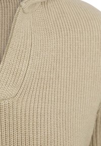 Beige gebreide cardigan met een V-hals en ribbelpatroon, gemaakt van een fijne, zachte draad en met een losse pasvorm.