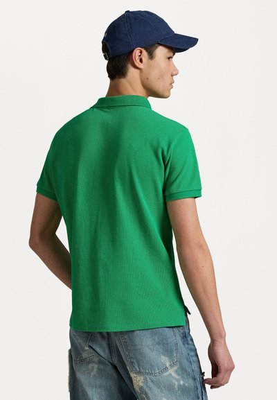 Zelena polo majica s kratkimi rokavi iz teksturirane tkanine in rebrastim ovratnikom, kombinirana z jeans kratkimi hlačami. Model nosi mornarsko kapo.
