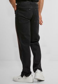Pantalones de mezclilla negros con un corte relajado, que cuentan con bolsillos traseros y una textura ligeramente desgastada. Combinados con zapatillas blancas.