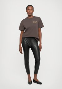 Brown cotton T-shirt with short sleeves and EA7 logo, paired with black faux leather leggings. Both items are fitted, sleek, and modern.
