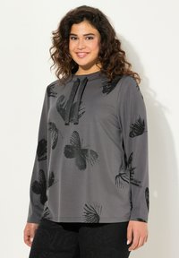 Maglietta grigia a maniche lunghe con stampe di farfalle nere, dotata di scollatura rotonda e lacci neri. Tessuto morbido e leggero con una texture liscia.