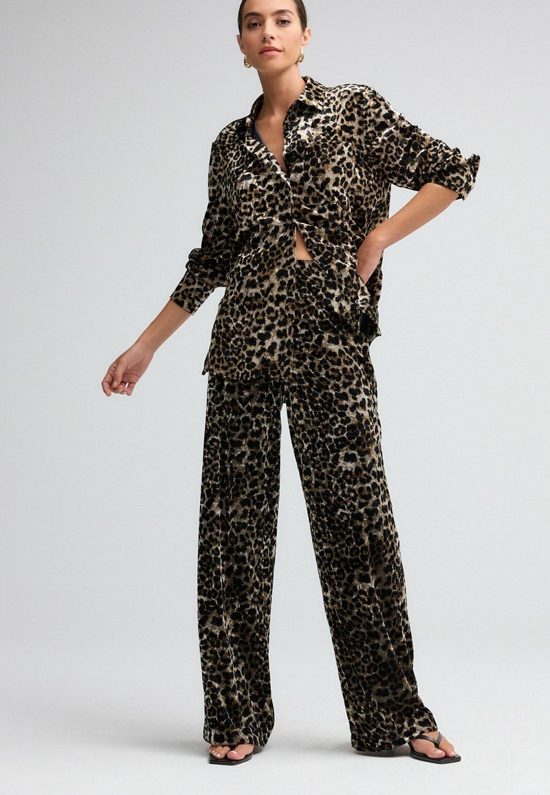 Pajamaset i leopardmönster tillverkat av mjukt tyg; innehåller en knäppbar skjorta med upprullade ärmar och löst sittande byxor med breda ben.