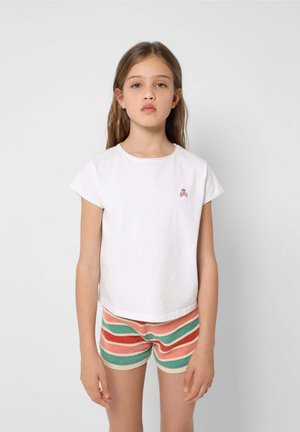 T-shirt bianca in cotone a maniche corte con un teschio rosa ricamato sul petto, abbinata a pantaloni corti a maglia a righe multicolori.