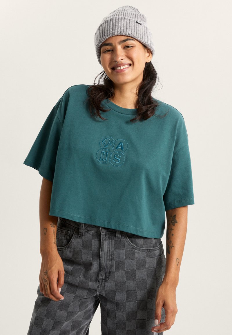 Tyrkist cropped t-shirt med korte ærmer og broderet design. Kombineret med sort ternede bukser og en grå ribbet hue.