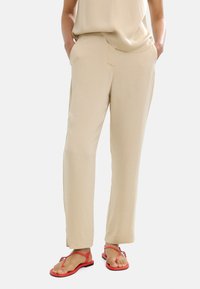 Beżowe spodni z dresówki o gładkiej fakturze, z bocznymi kieszeniami i prostym krojem, zestawione z płaskimi czerwonymi sandałami.