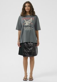 Grå oversized t-shirt med grafisk print, parret med en sort nederdel med palietter. Flade sandaler fuldender outfittet.