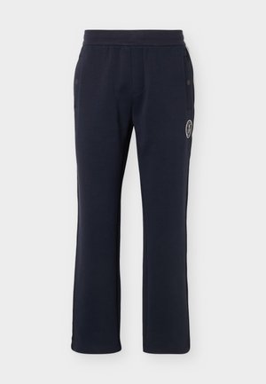 Μπλε σκούρο φόρμα με ελαστική μέση, πλαϊνές τσέπες με κουμπιά και λευκό κυκλικό λογότυπο στο δεξί μηρό.