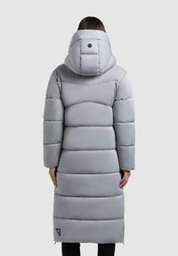 Lungo cappotto grigio imbottito con cappuccio, dotato di un design trapuntato e chiusura frontale con zip. Presenta un dettaglio del logo nero sul fondo.