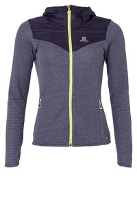 Lila jacka med en mörklila huva och en grön dragkedja. Har lång ärm, dragkedjefickor och en texturerad tygdesign.