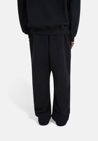 Sorte joggebukser laget av mykt stoff, med en avslappet passform, elastisk midje og mansjetter ved anklene. Enkel, ensartet tekstur.