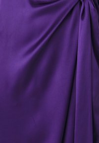 Violetinė audinio užuolaida su lygiu paviršiumi, sukurianti susirinkusių skyrių ir tekančio dizaino efektą, pabrėžianti turtingą spalvą ir minkštą išvaizdą.