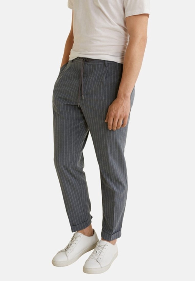Pantalones de rayas grises en un material ligero con un ajuste tapered, que cuentan con una cintura con cordón y dobladillos ajustados, combinados con zapatillas blancas.