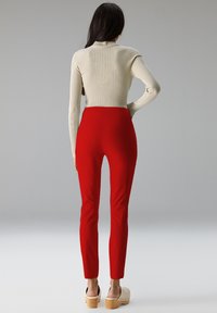Rode, aansluitende broek met een hoge taille, gecombineerd met een crèmekleurig, geribd shirt met lange mouwen. De outfit heeft een soepel, rekbaar stof en houten platform schoenen.