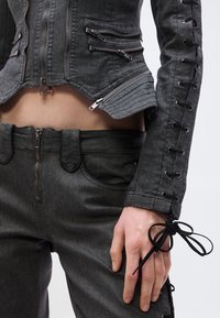 Hall hall teksariidest jakk, millel on mitu tõmblukku ja pits-kirjeldus varrukatel, kombineeritud sobivate kõrge vöökohaga pükstega, mille keskel on tõmblukk.