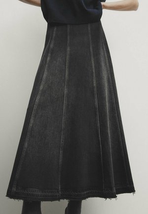 Sort denim A-line nederdel med lodrette sømdetaljer og rå kant, båret med mørk top og støvler, vist fra talje til ankler.