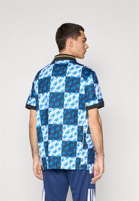 Poloshirt mit kurzen Ärmeln in einem blau-schwarzen geometrischen Muster, mit einem schwarzen Kragen und gelben Akzenten. Hergestellt aus leichtem Stoff.