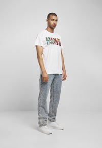 Hvid bomulds T-shirt med et farverigt grafisk print, der staver "MARVEL." Bæres med lyseblå, slidte denimjeans og hvide sneakers.