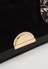 Sac noir en tissu texturé avec un fermoir doré en demi-cercle gravé "ALDO" près du bord inférieur.