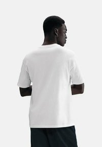 Hvid kortærmet t-shirt, rund halsudskæring, blødt stof, afslappet pasform, båret bagfra, med en enkelt, glat tekstur mod en lys grå baggrund.