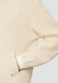 Gequilted crèmekleurig sweatshirt met een gestructureerd oppervlak, geribbelde witte manchet en een zijzak. Bevat een subtiel geborduurd logo nabij de zak.