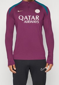 Uomo che indossa una maglia da calcio viola del Paris Saint-Germain con il logo di Qatar Airways e pantaloni neri Nike con il logo bianco dello swoosh.