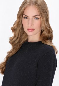 Pull en maille bleu marine à col rond, présentant un tissu texturé avec de subtiles nuances de bleu partout. Manches longues visibles.