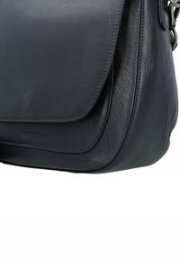 Primo piano di una borsa in pelle di colore blu scuro con chiusura a pattina, bordi arrotondati e fine dettaglio di cucitura.