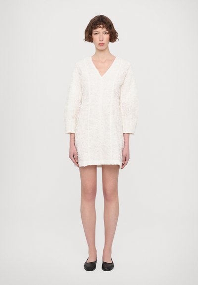 Weißes Kleid mit V-Ausschnitt und Dreiviertelärmeln, strukturiertes Blumenmuster, oberhalb des Knies, kombiniert mit schwarzen Ballerinas.