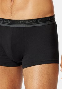 Boxer-briefs noirs en tissu doux, dotés d'une ceinture noire avec le logo gris "uncover", et un ajustement serré autour des cuisses.