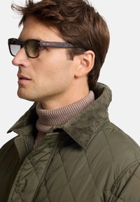 Occhiali da vista tartarugati marroni, giacca trapuntata verde oliva e dolcevita rosa chiaro a costine. Dettaglio notevole del colletto e tessuto strutturato.