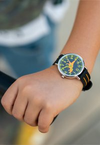 Montre en silicone noire avec des accents orange, cadran rond, fond bleu, chiffres jaunes et un design ludique représentant la silhouette d'un animal.