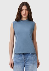 Top senza maniche in cotone blu con collo alto, texture liscia e taglio rilassato, abbinato a jeans azzurri.