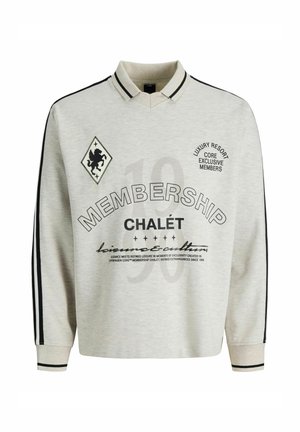 Polo à manches longues gris clair avec des rayures noires sur les manches, détail du col, et texte imprimé incluant "MEMBERSHIP CHALÉT" ainsi qu'un emblème de lion.