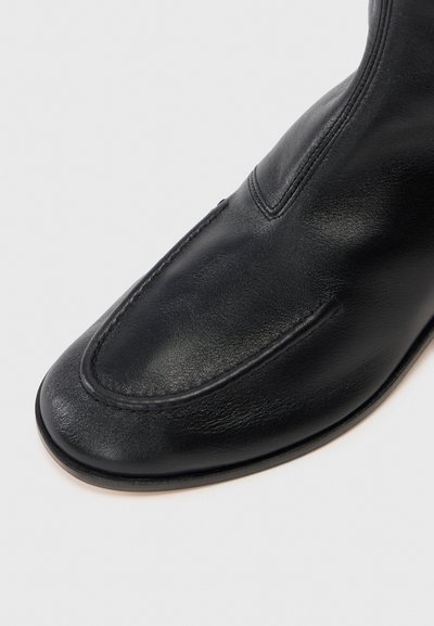 Černá kožená kotníková bota s kulatou špičkou, s hladkým povrchem a viditelným stehem podél svršku. Klasický design, minimalistický styl.