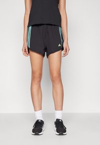 Bermudas deportivas negras con rayas turquesas y acentos de logo verde, hechas de un tejido ligero. Combinadas con zapatillas negras y calcetines blancos.