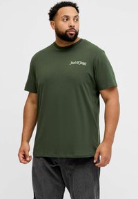 Camiseta de algodón de color verde oliva con mangas cortas, que presenta un pequeño logotipo blanco en el lado izquierdo del pecho. Diseño clásico con cuello redondo.