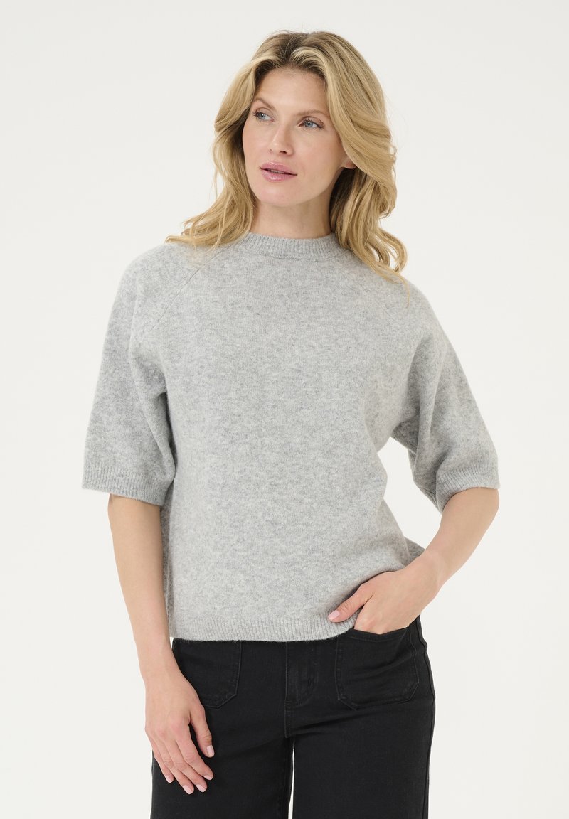Lichtgrijze, korte mouwen trui met een ronde hals en een tekstuurstof. Gecombineerd met zwarte jeans met zijzakken.