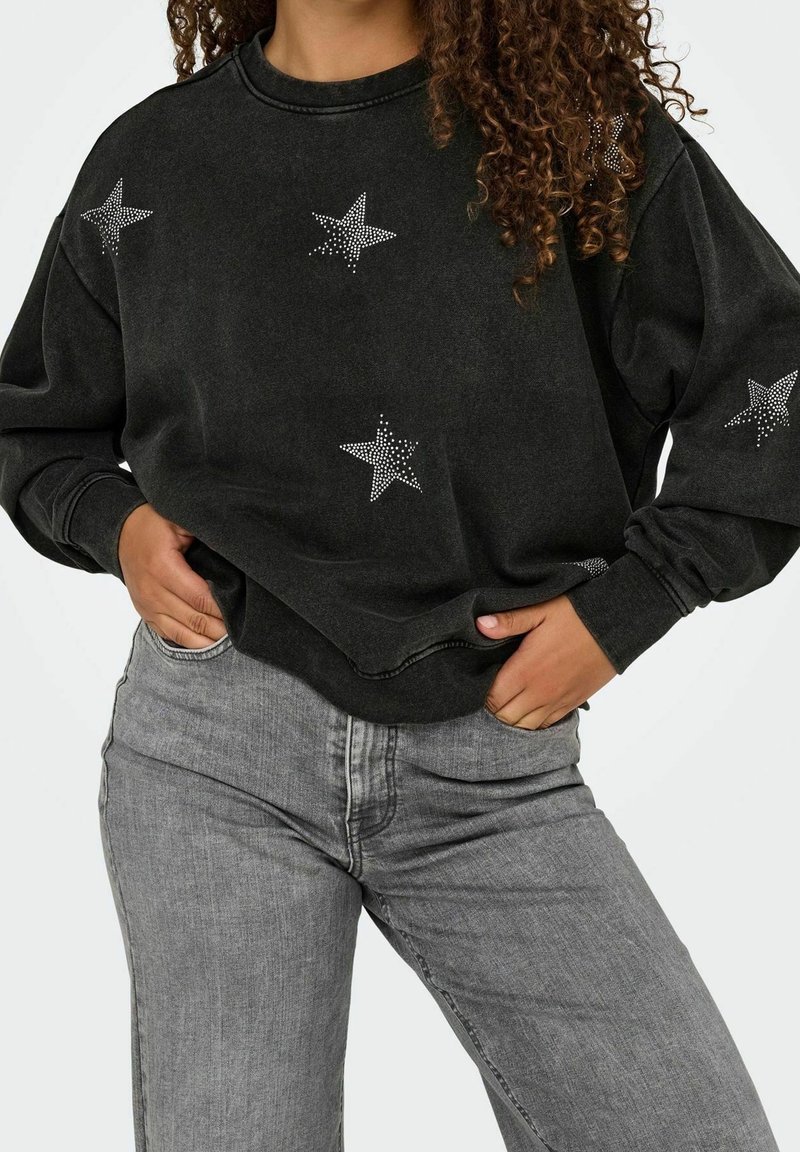 Sweat-shirt noir avec des embellissements en forme d'étoiles argentées, col rond, manches longues et coupe décontractée, associé à un jean gris clair.
