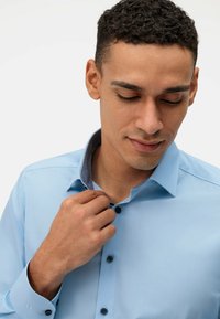 Chemise bleu clair avec un col étalé et un détail de col intérieur gris. Présente une fermeture à boutons et une texture de tissu lisse.