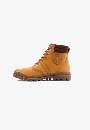 Stivale alla caviglia in pelle tan con collo in suede marrone, occhielli in metallo e suola in gomma con punte di trazione. Logo impresso sul lato esterno.