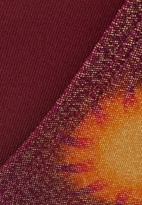 Bordeauxfärgad textil med en strukturerad, gradientkant som övergår till orange och guld. Har synlig sömnad som skapar en jämn, lager-på-lager design.