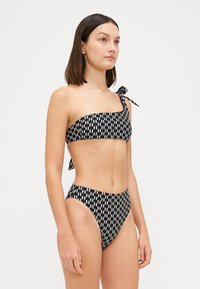 Fekete-fehér mintás bikini, bal oldalon megkötött, egy vállpánttal; magasan fazonú alsó; sima anyagtextúra.