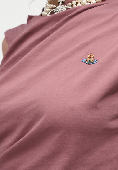 Mauve-värinen puuvillainen t-paita, jossa on kirjailtu pieni vene sinisessä ympyrässä. Sileä pinta ja rento istuvuus.